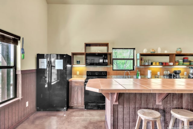 723 Tierra Linda, Concan, TX 78838 - kitchen with tile counters, open shelves, black appliances, a kitchen bar, and concrete flooring