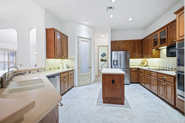 kitchen featuring visible vents, a kitchen island, a sink, stainless steel appliances, and decorative backsplash