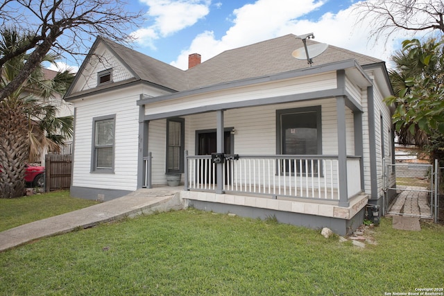 view of front facade with a front yard, a porch, fence, and a chimney