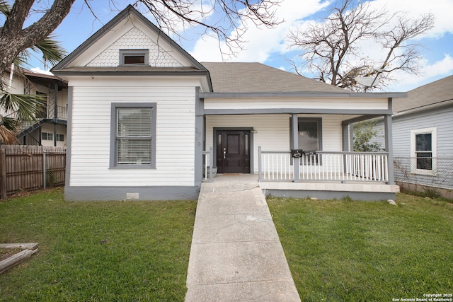 view of front of house with a shingled roof, covered porch, fence, and a front lawn