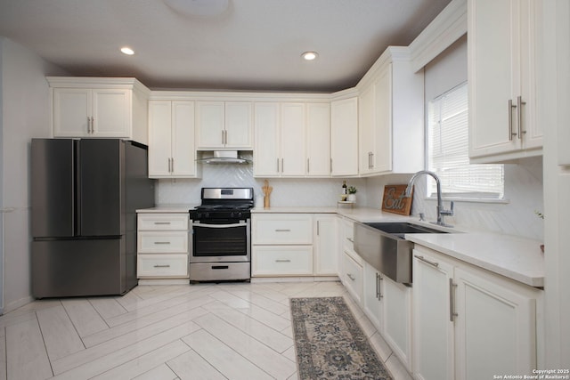 kitchen with freestanding refrigerator, stainless steel range with gas cooktop, backsplash, under cabinet range hood, and a sink