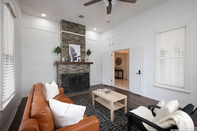 living area featuring a fireplace, a ceiling fan, visible vents, wood finished floors, and baseboards