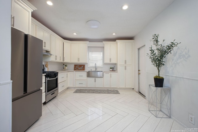 kitchen with recessed lighting, light countertops, under cabinet range hood, stainless steel appliances, and a sink