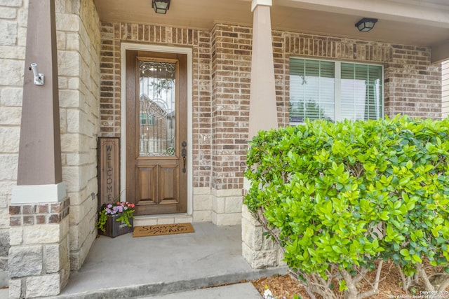 view of exterior entry featuring a porch, brick siding, and stone siding
