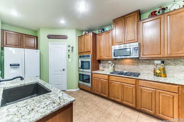 kitchen with backsplash, stainless steel appliances, light stone countertops, and a sink