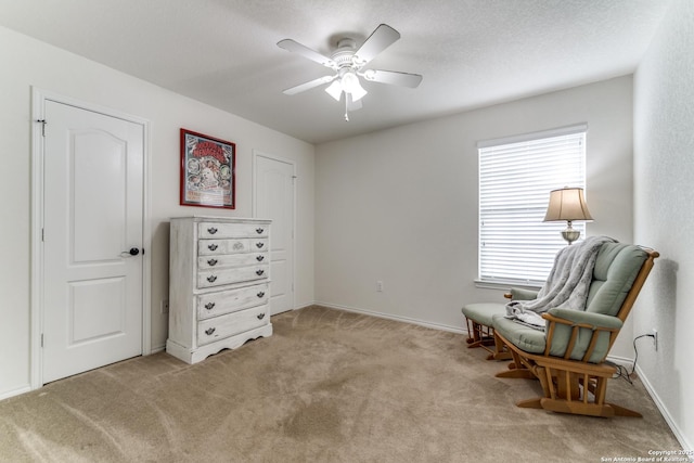 living area featuring baseboards, a ceiling fan, and light colored carpet