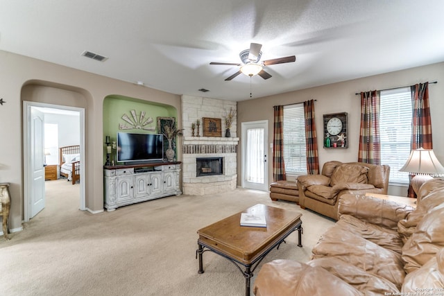 living room featuring ceiling fan, light colored carpet, a stone fireplace, and visible vents