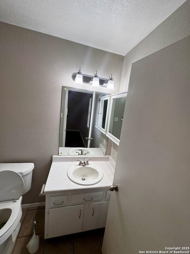 bathroom with toilet, a textured wall, a textured ceiling, vanity, and tile patterned floors