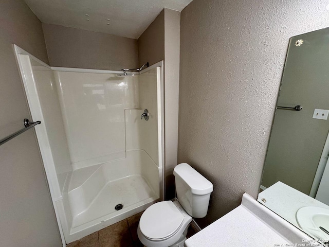 bathroom with toilet, a walk in shower, vanity, and a textured wall