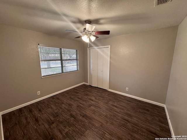 unfurnished bedroom with a closet, baseboards, dark wood-style floors, and visible vents