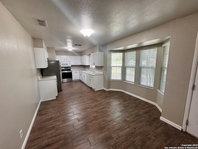 kitchen featuring white microwave, stainless steel range with electric cooktop, freestanding refrigerator, dark wood finished floors, and visible vents