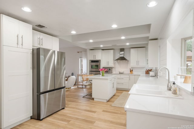 kitchen featuring wall chimney range hood, a sink, stainless steel appliances, white cabinetry, and visible vents