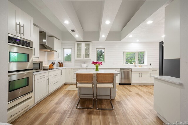 kitchen with wall chimney range hood, tasteful backsplash, stainless steel appliances, white cabinets, and visible vents