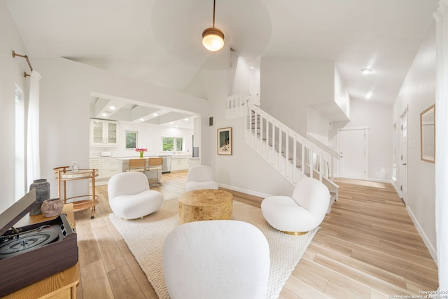 living area with light wood-type flooring, baseboards, high vaulted ceiling, and stairway