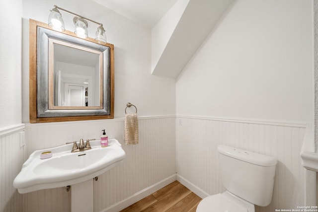 half bath with wood finished floors, toilet, a sink, and wainscoting
