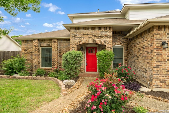 entrance to property with fence, brick siding, and roof with shingles