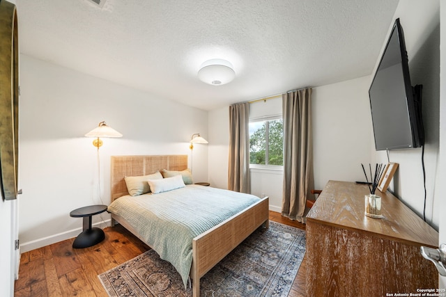 bedroom with wood finished floors, a textured ceiling, and baseboards