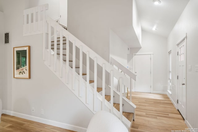 stairway featuring high vaulted ceiling, wood finished floors, visible vents, and baseboards