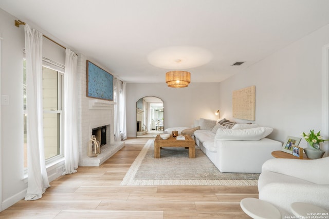 living area with light wood-style floors, arched walkways, baseboards, a brick fireplace, and visible vents