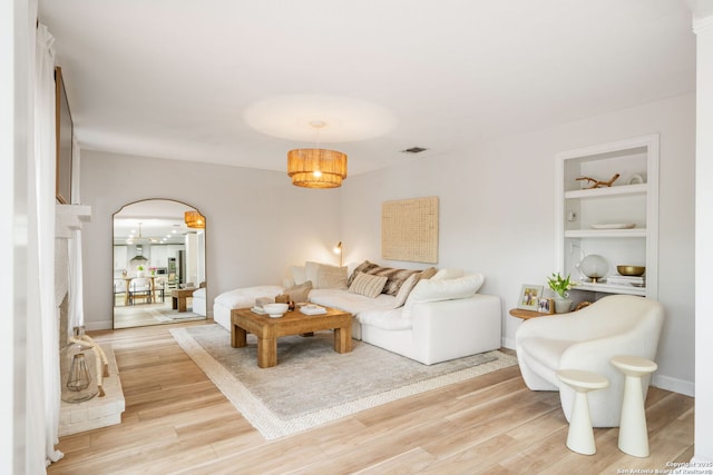 living room with visible vents, arched walkways, light wood-style floors, and built in shelves
