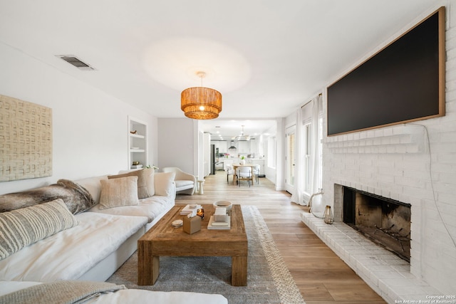 living area featuring a fireplace, light wood-type flooring, visible vents, and built in features