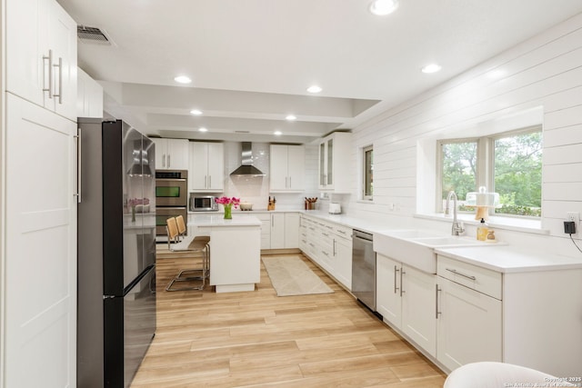 kitchen featuring a sink, backsplash, wall chimney exhaust hood, appliances with stainless steel finishes, and visible vents