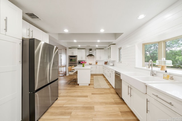 kitchen featuring white cabinets, wall chimney range hood, visible vents, a sink, and appliances with stainless steel finishes