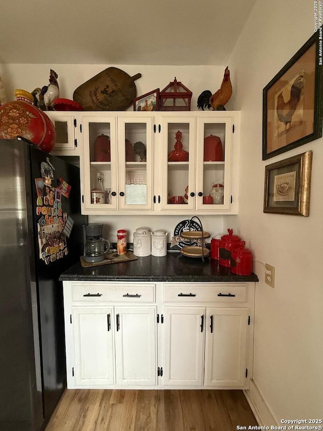 kitchen featuring glass insert cabinets, white cabinets, dark countertops, freestanding refrigerator, and wood finished floors