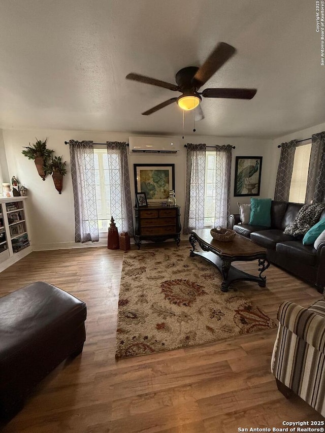 living room with a wall unit AC, wood finished floors, baseboards, and a ceiling fan