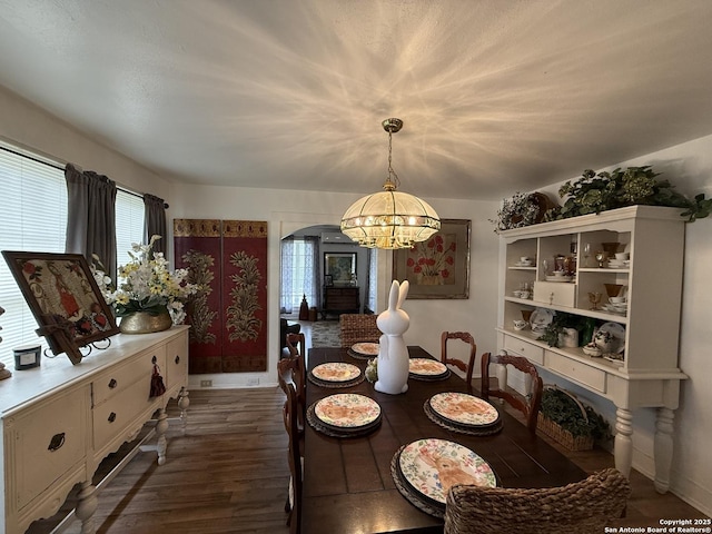 dining room featuring baseboards, arched walkways, a notable chandelier, and dark wood finished floors