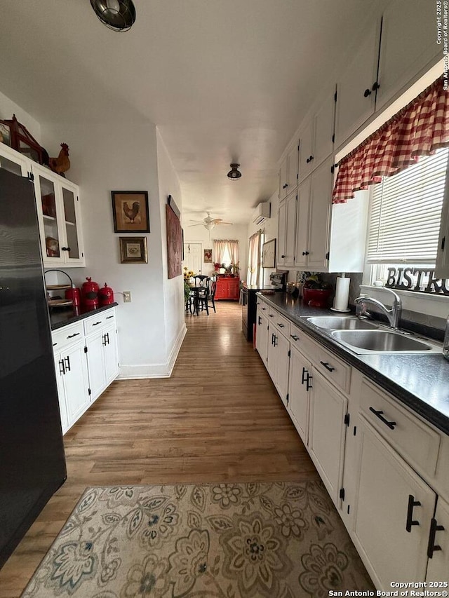 kitchen with white cabinets, a sink, freestanding refrigerator, dark countertops, and wood finished floors