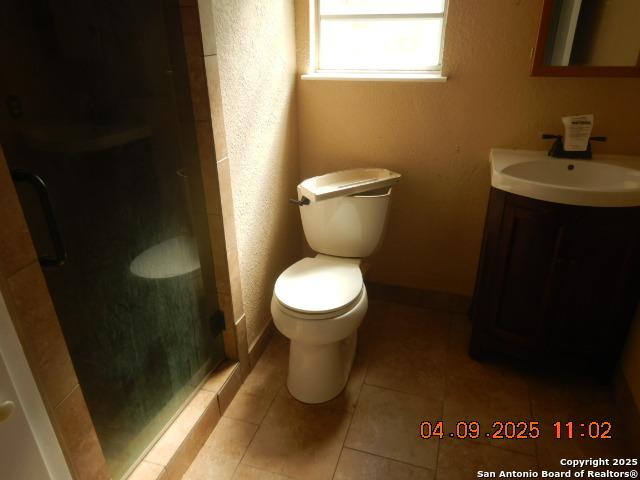 9704 Big Geronimo, San Antonio, TX 78254 - bathroom with baseboards, toilet, vanity, tile patterned flooring, and a stall shower