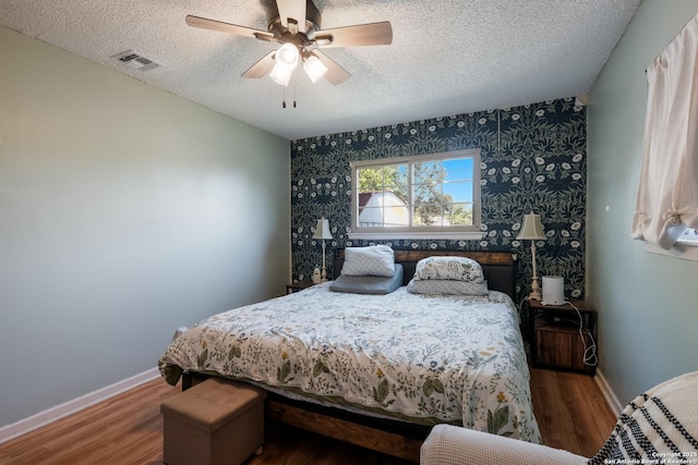 bedroom featuring visible vents, baseboards, a ceiling fan, a textured ceiling, and wood finished floors