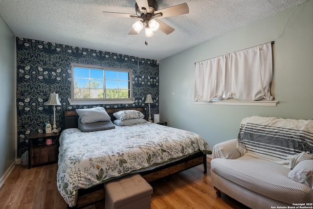 bedroom with baseboards, wallpapered walls, a textured ceiling, ceiling fan, and wood finished floors