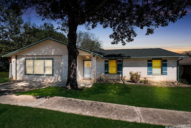 single story home with a yard, a shingled roof, and brick siding
