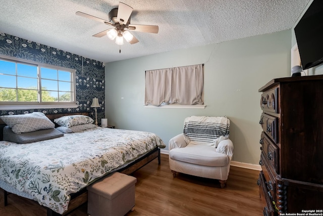 bedroom featuring baseboards, wallpapered walls, a textured ceiling, a ceiling fan, and wood finished floors