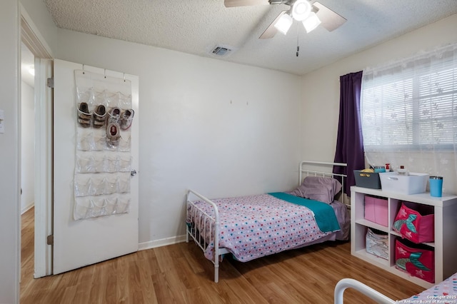 bedroom featuring a textured ceiling, wood finished floors, ceiling fan, and visible vents
