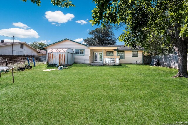 back of house featuring a trampoline, french doors, a fenced backyard, and a lawn