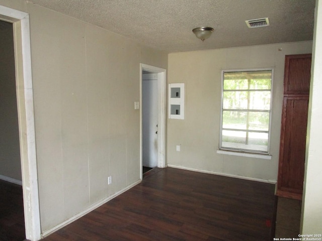 empty room featuring a textured ceiling, wood finished floors, baseboards, and visible vents