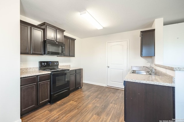 kitchen with dark brown cabinetry, black appliances, dark wood-style flooring, light countertops, and a sink