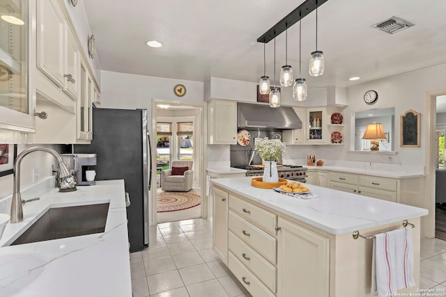 kitchen featuring range hood, visible vents, a sink, light tile patterned flooring, and glass insert cabinets