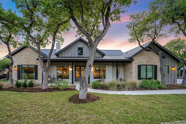 modern farmhouse style home with a standing seam roof, stone siding, metal roof, and a lawn