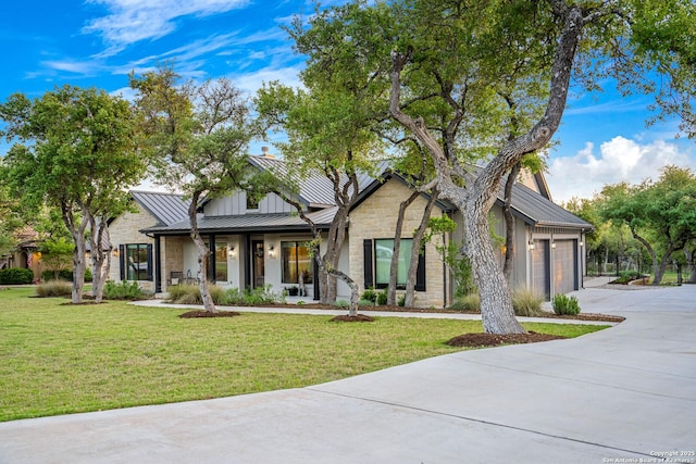 modern farmhouse featuring stone siding, metal roof, concrete driveway, a front lawn, and a standing seam roof