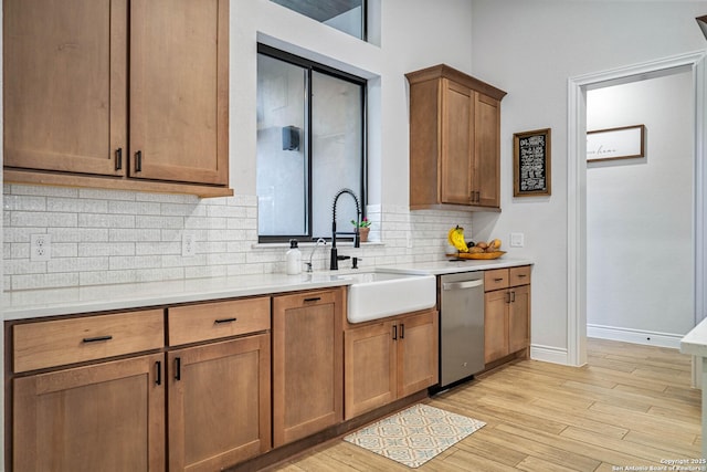 kitchen with a sink, light countertops, light wood finished floors, backsplash, and stainless steel dishwasher