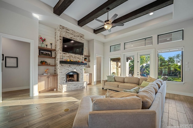 living area featuring light wood-type flooring, a stone fireplace, french doors, baseboards, and beam ceiling