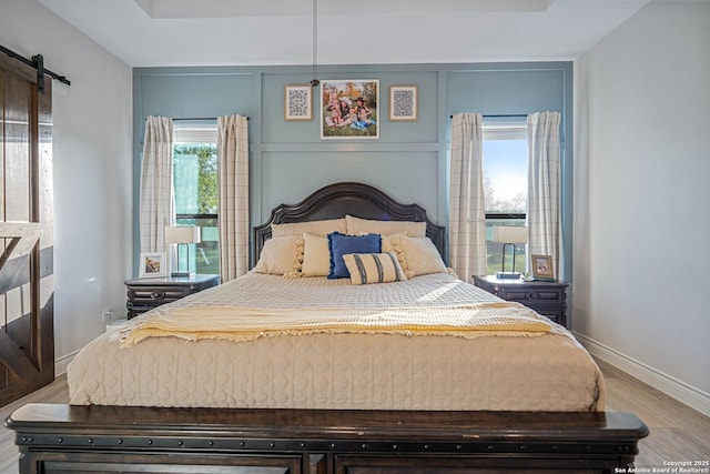 bedroom featuring a tray ceiling, baseboards, a barn door, and wood finished floors