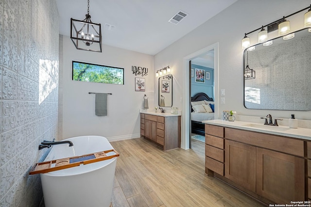 ensuite bathroom featuring a sink, visible vents, two vanities, and wood finished floors