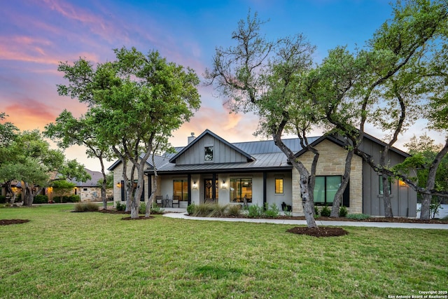 modern inspired farmhouse featuring a yard, stone siding, metal roof, and a standing seam roof