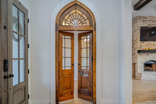 entrance foyer with baseboards, french doors, a brick fireplace, arched walkways, and wood finished floors