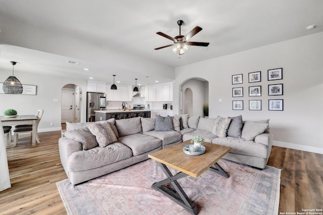 living area with arched walkways, light wood finished floors, baseboards, and a ceiling fan